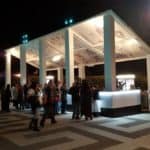 Thumbnail of http://Side%20view%20Crowds%20gather%20at%20mobile%20food%20cart%20and%20bar%20kiosk%20on%20sloped%20ground%20at%20the%20Greek%20Theater